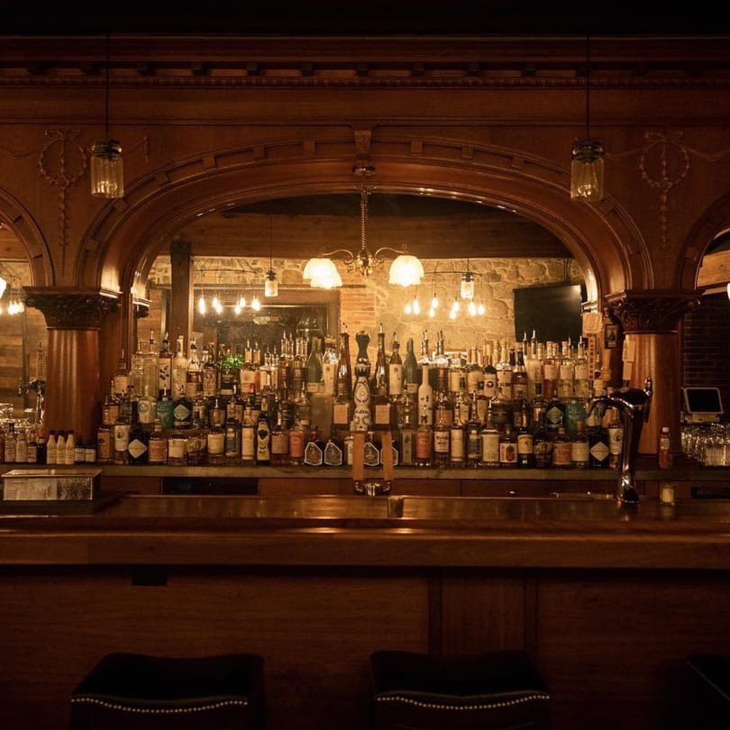 Stone House bar with a large selection of liquor bottles, ornate wooden archways, and warm lighting.