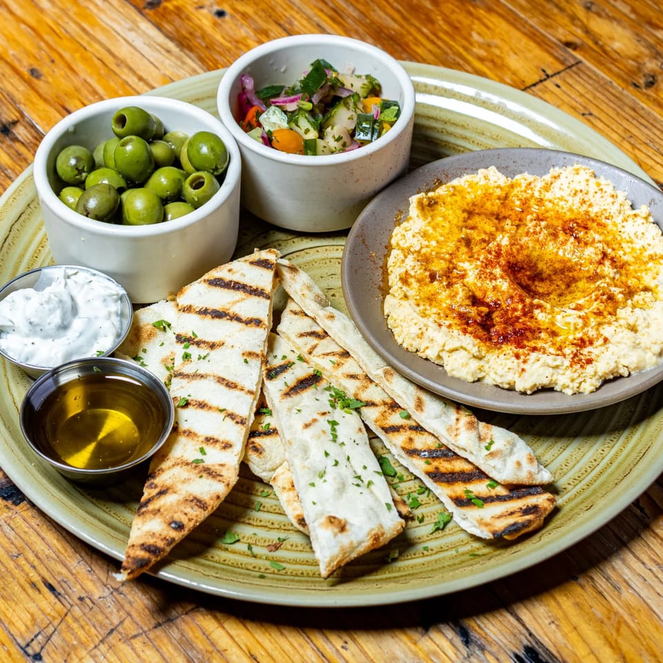 A Stone House appetizer platter with hummus, grilled flatbread, olives, salsa, olive oil, and tzatziki.