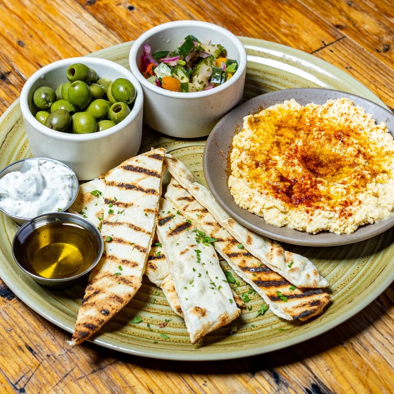 A Stone House appetizer platter with hummus, grilled flatbread, olives, salsa, olive oil, and tzatziki.