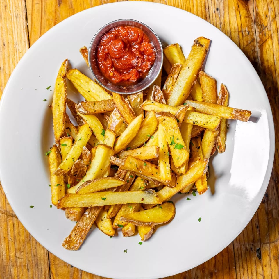 Golden-brown french fries with seasoning and a side of red ketchup on a white plate.