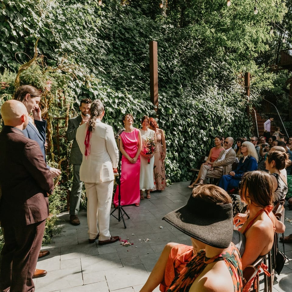 Outdoor wedding ceremony at Stone House, with guests seated and the wedding party standing among lush greenery.