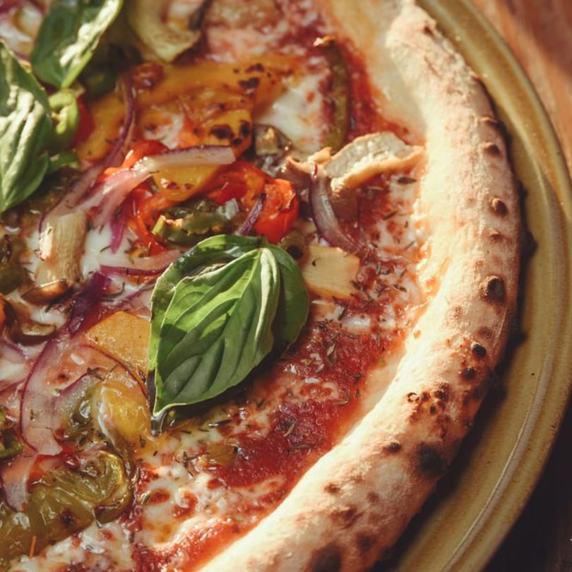 Close-up of a Stone House pizza with roasted vegetables, red sauce, cheese, and fresh basil.