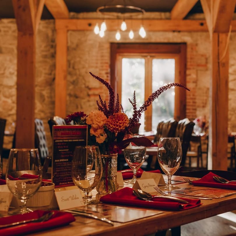 A Stone House dining table set with red napkins, wine glasses, and a floral centerpiece.