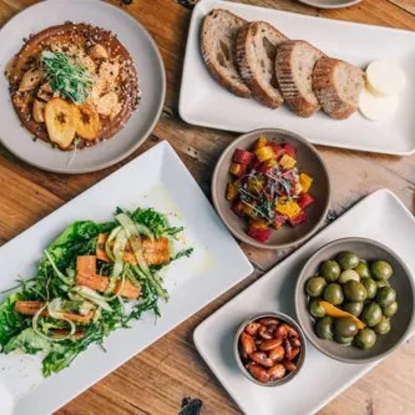 Overhead view of Stone House New American dishes: salad, bread, olives, nuts, and a dessert.