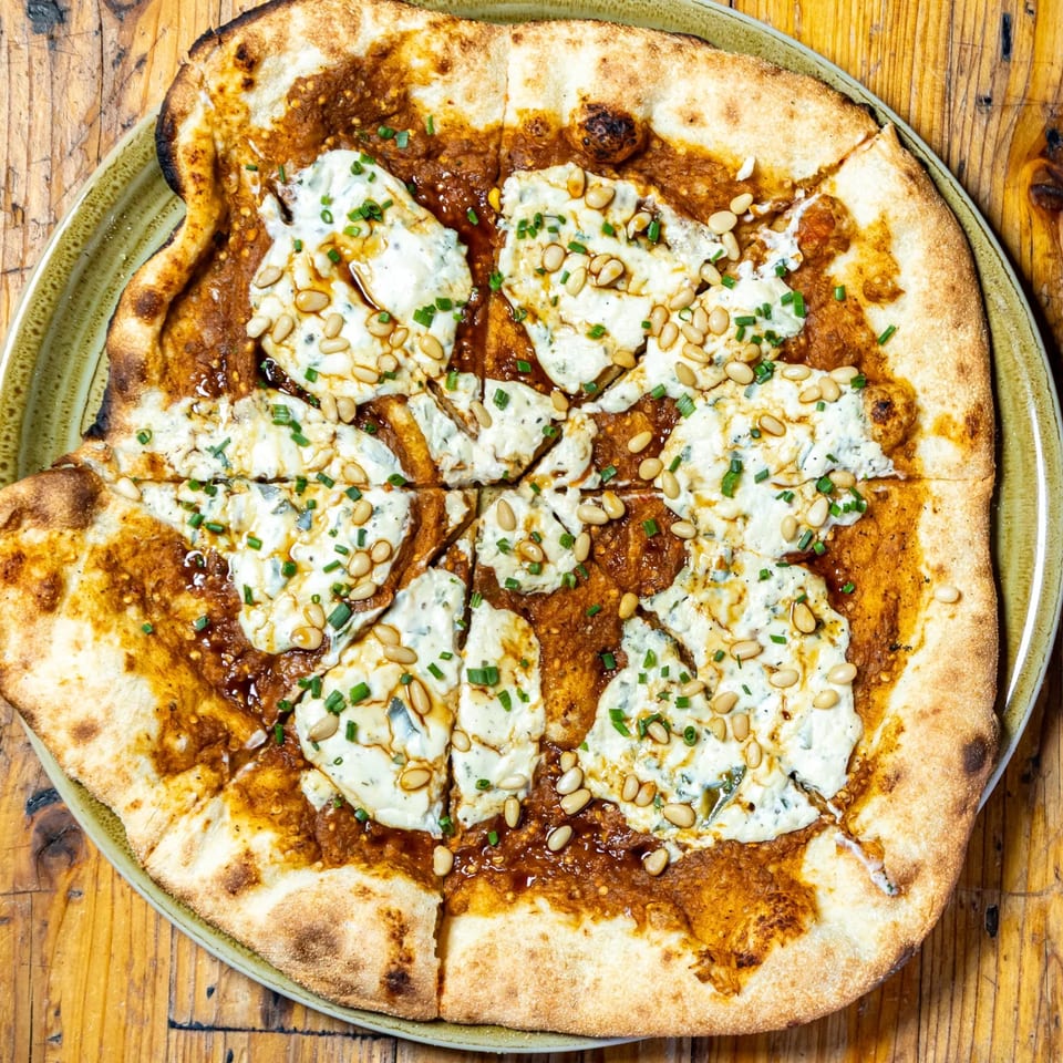 Stone House New American pizza with white sauce, red sauce, pine nuts, and chives.