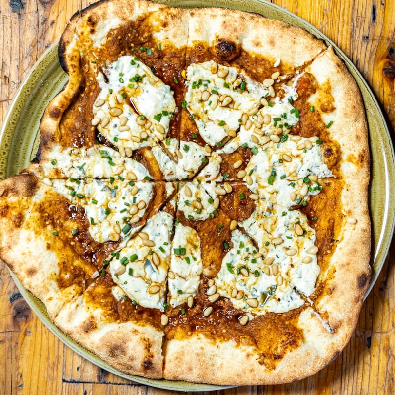 Stone House New American pizza with white sauce, red sauce, pine nuts, and chives.