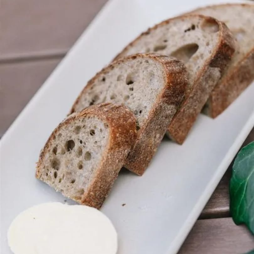 Slices of fresh, crusty bread with a pat of butter on a white rectangular plate.