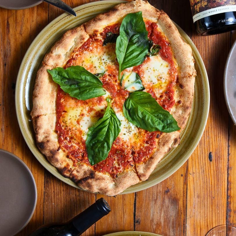Stone House's New American Margherita pizza with fresh basil, mozzarella, and tomato sauce on a wooden table.