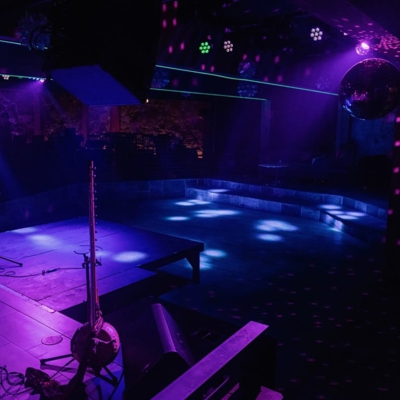 A dark, empty Stone House stage and dance floor illuminated by purple and green lights.