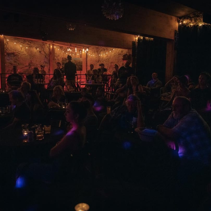 Patrons enjoying a dimly lit evening at Stone House, with string lights illuminating a stone wall.