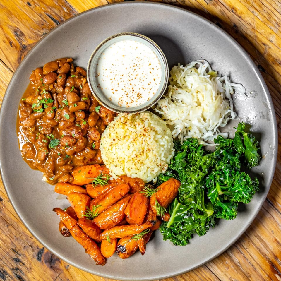 A Stone House New American dish with beans, rice, carrots, kale, sauerkraut, and a creamy sauce.