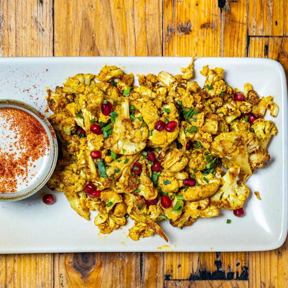 Roasted cauliflower with pomegranate seeds, green onions, and a side of white sauce with paprika.