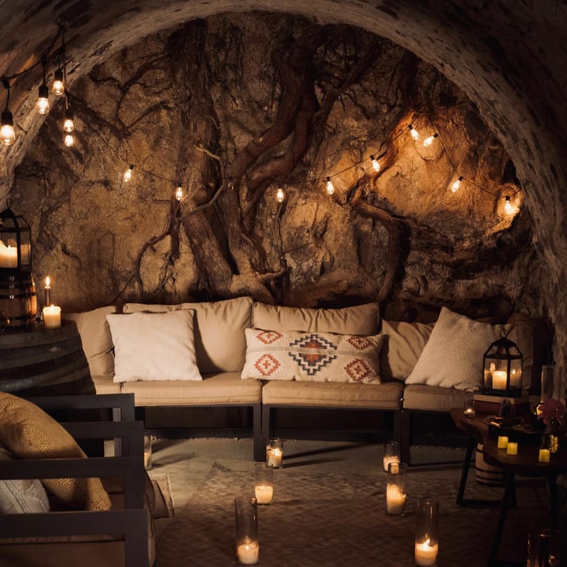 A cozy, dimly lit cave-like room with string lights, candles, and comfortable seating at Stone House.