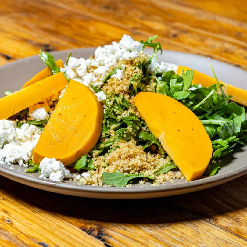 Stone House's butternut squash salad with arugula, crumbled feta, and toasted breadcrumbs on a wooden table.
