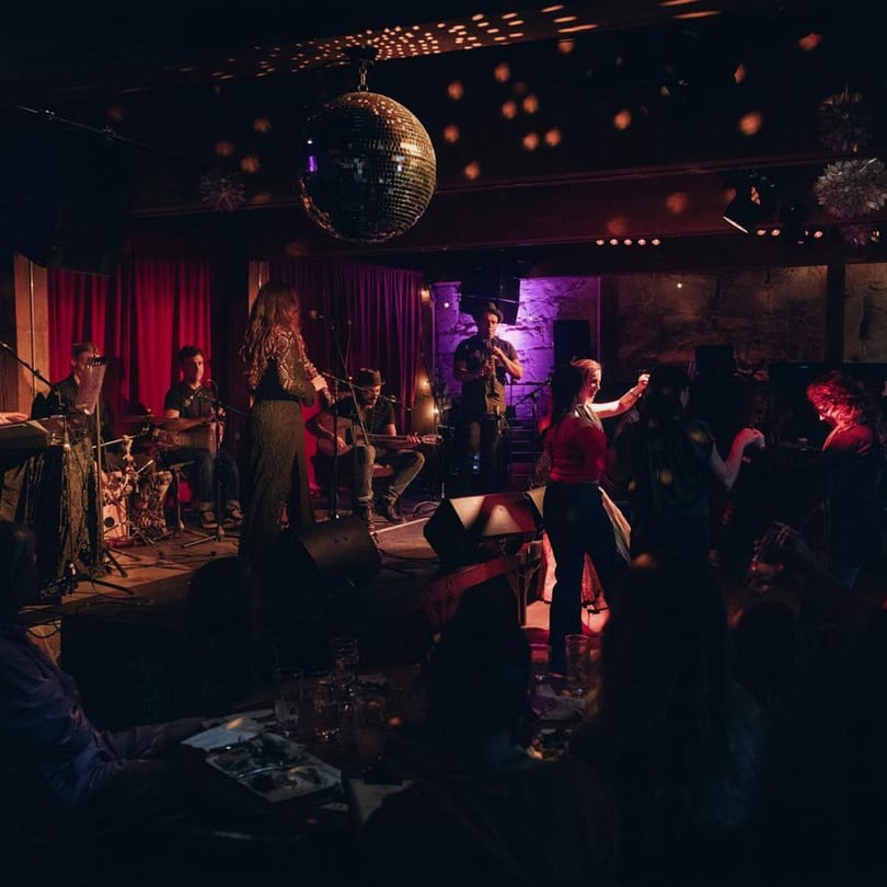 A band performs on stage under a disco ball, with patrons dancing and enjoying the music.