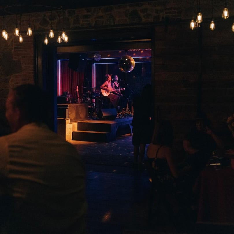 Live music performance at Stone House, with two musicians on stage and patrons watching in the foreground.