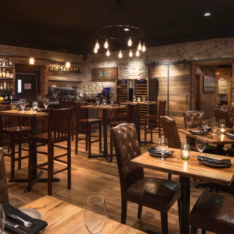 The Stone House restaurant interior features rustic wood tables, leather chairs, and stone walls under warm lighting.