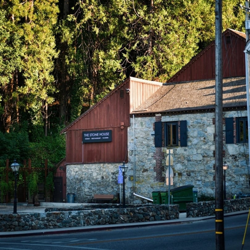 The Stone House restaurant, a rustic stone and wood building, nestled among lush green trees.