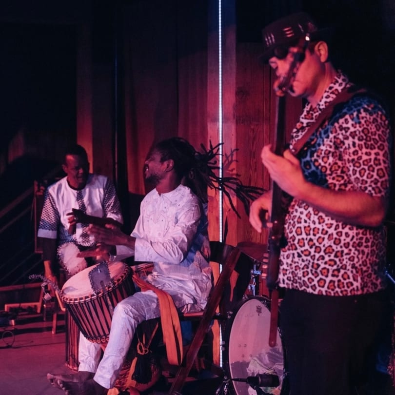 Three musicians performing with drums and a guitar on a dimly lit stage at Stone House.