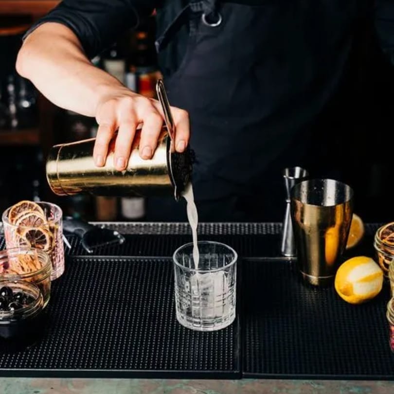 Bartender pouring a white cocktail from a golden shaker into a glass with ice at Stone House.