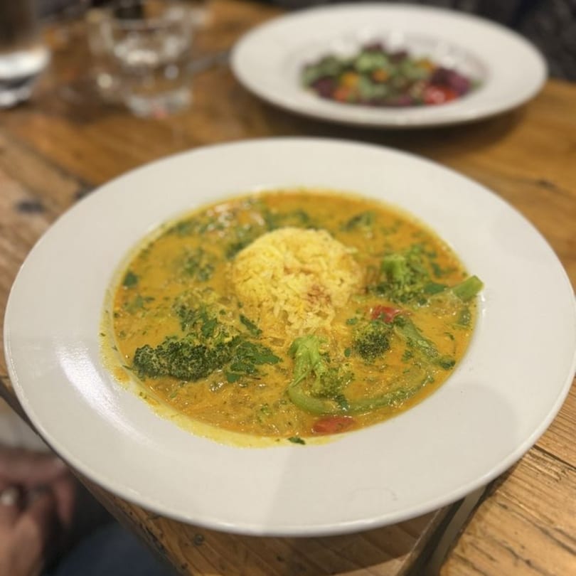 A bowl of yellow curry with broccoli, red peppers, and a scoop of rice at Stone House.