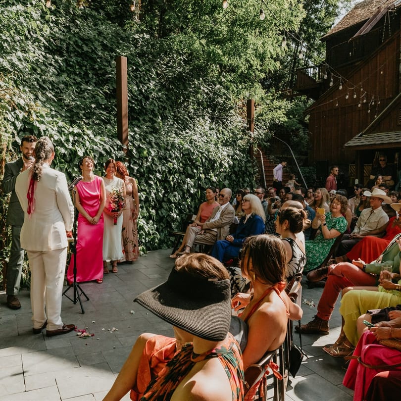 Outdoor wedding ceremony at Stone House, with guests seated and the wedding party standing before lush greenery.