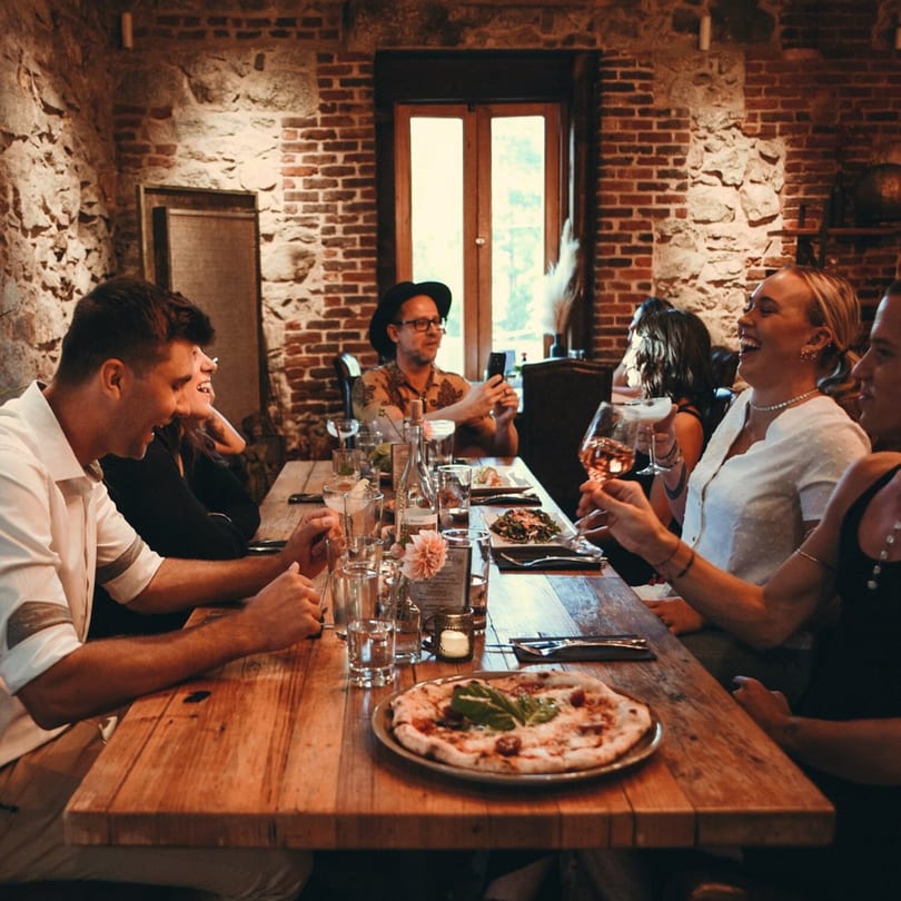 Friends enjoying dinner and drinks at a long wooden table in Stone House restaurant.