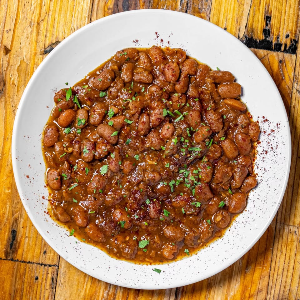 Hearty baked beans in a rich brown sauce, garnished with fresh parsley on a white plate.