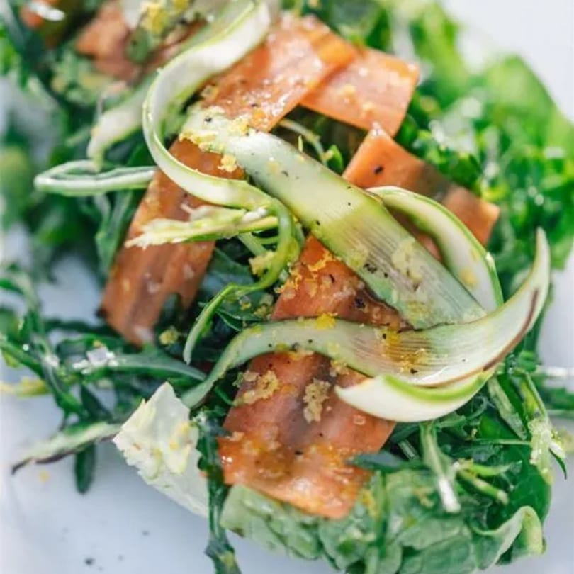 Close-up of a fresh salad with green leaves, orange slices, and shaved asparagus.