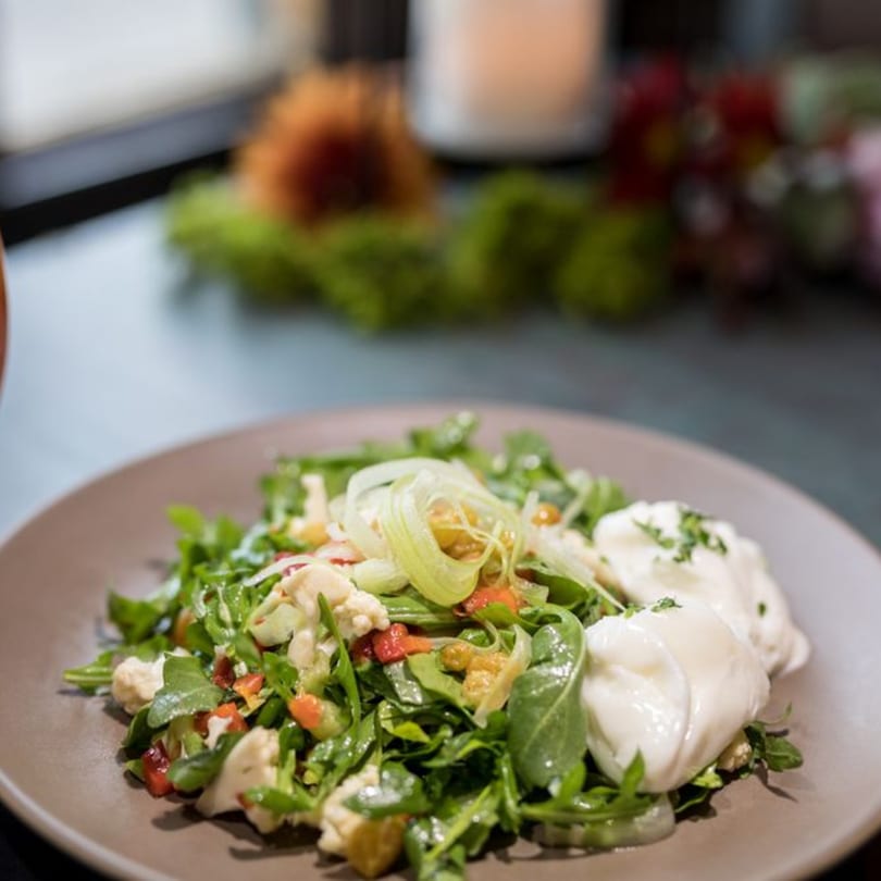 A Stone House New American salad with greens, vegetables, and burrata cheese on a brown plate.