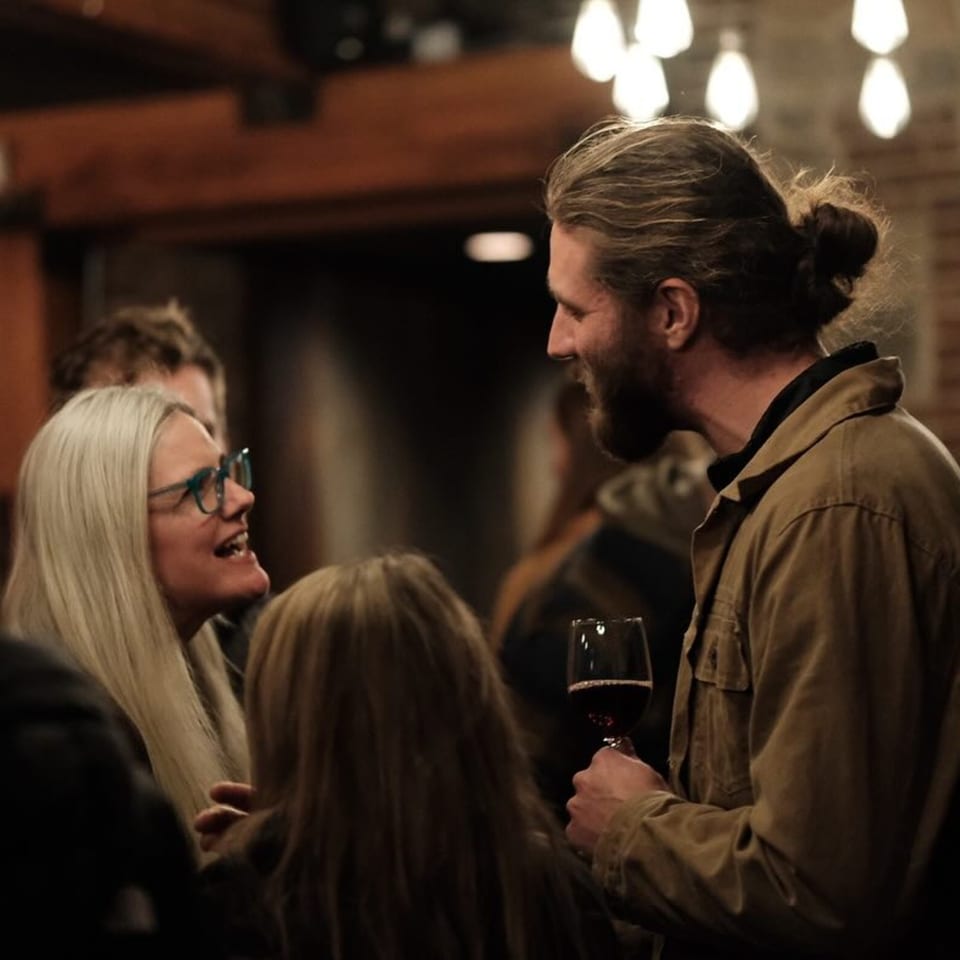 Guests socializing at Stone House, a man with a beard holding a glass of red wine.