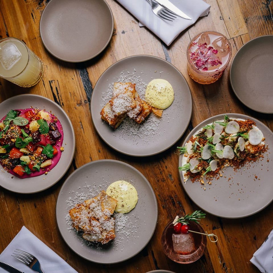 Overhead view of Stone House's New American dishes and cocktails on a rustic wooden table.