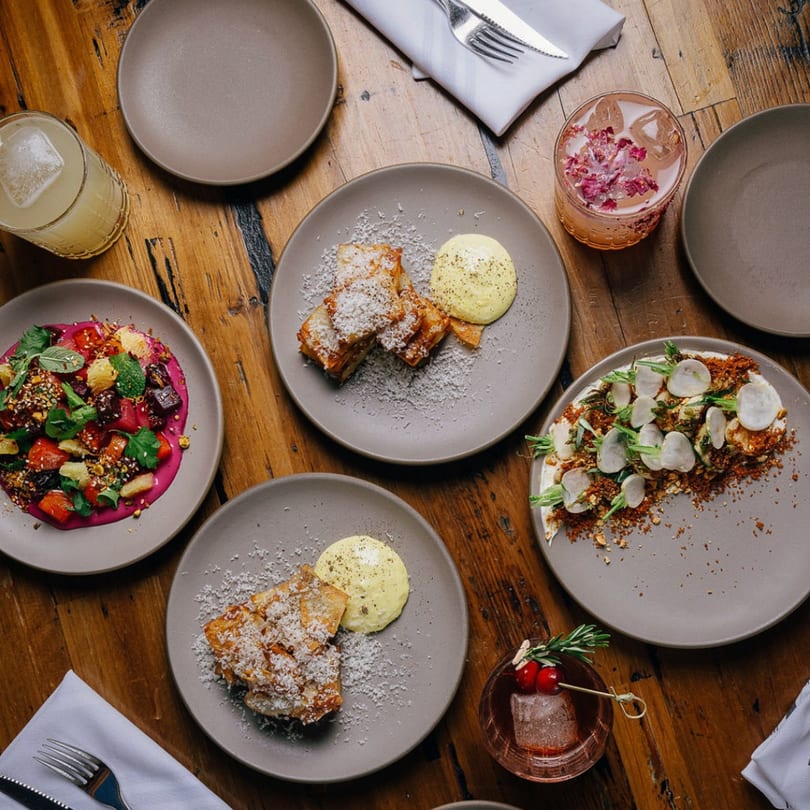 Overhead view of Stone House's New American dishes and cocktails on a rustic wooden table.