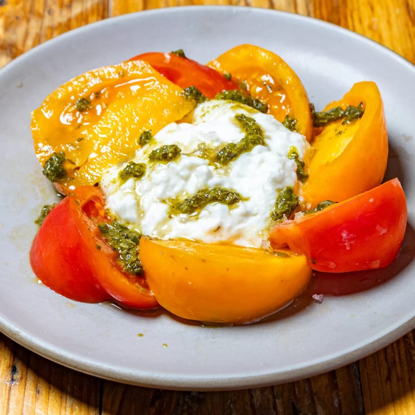 Heirloom tomato salad with burrata cheese and pesto on a white plate at Stone House.