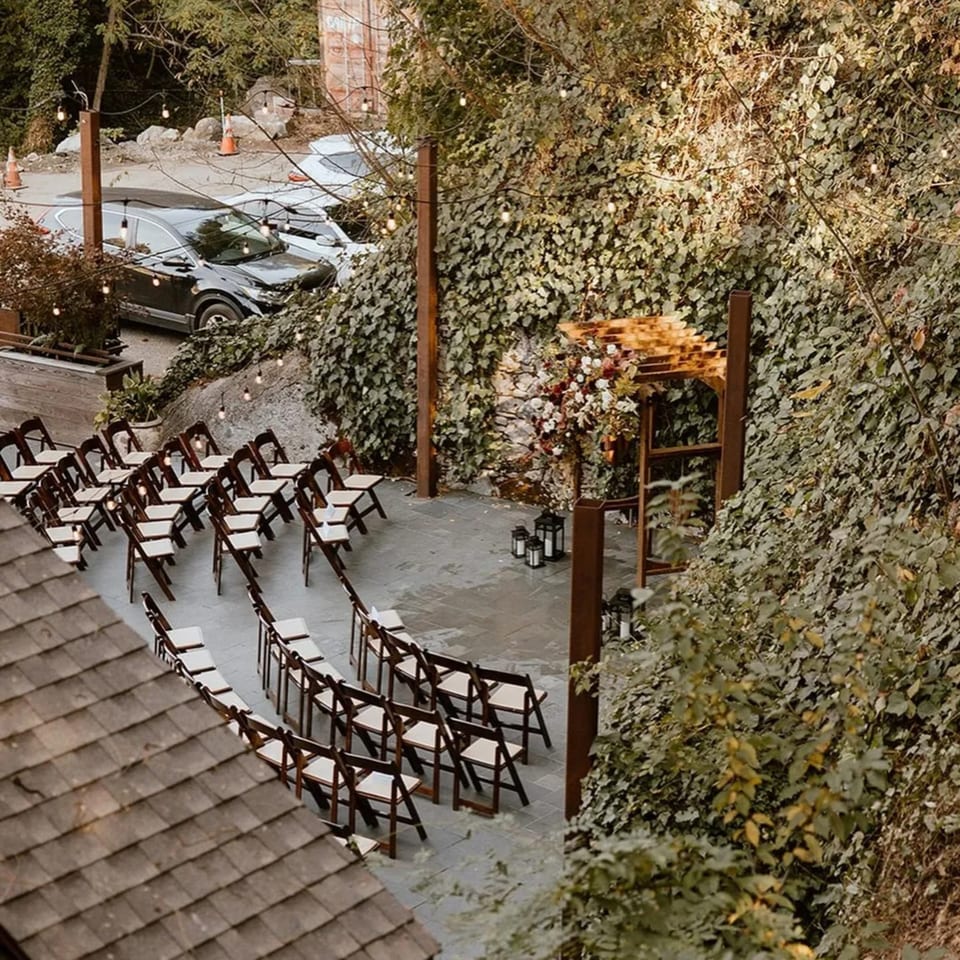 Outdoor ceremony setup with rows of chairs, a floral arch, and string lights at Stone House.