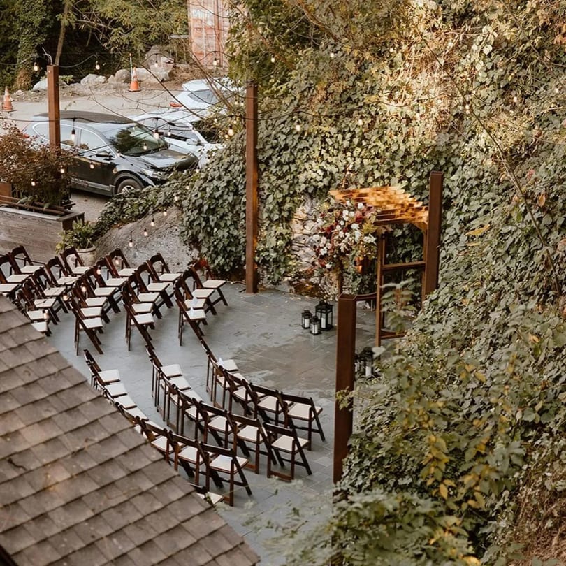 Outdoor ceremony setup with rows of chairs, a floral arch, and string lights at Stone House.