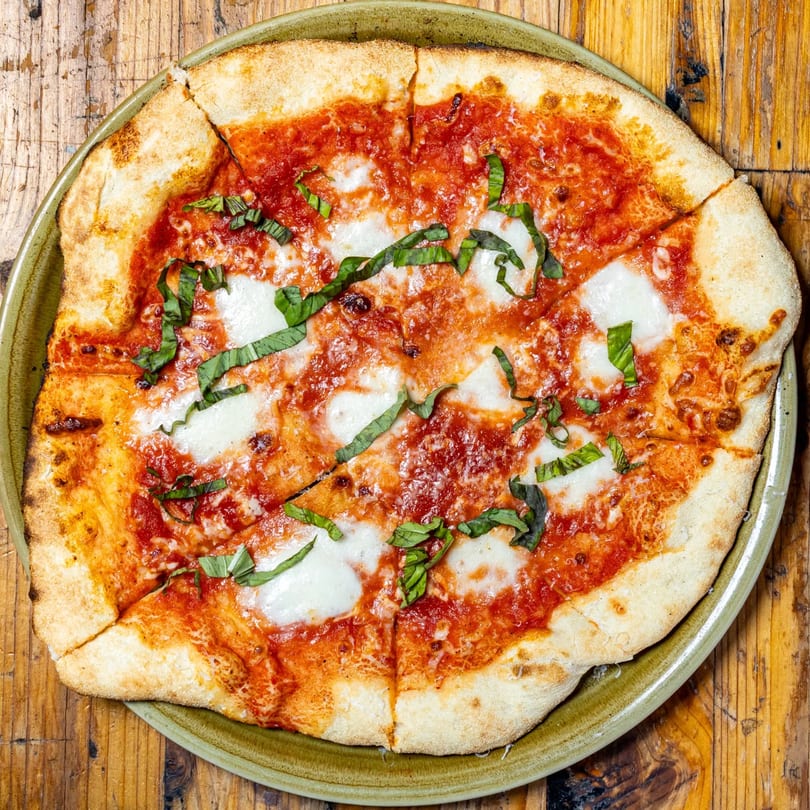 A New American Margherita pizza, sliced into eight pieces, on a green plate atop a wooden table.