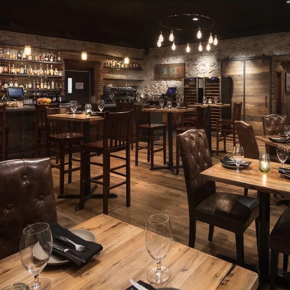 The Stone House restaurant interior features a rustic bar, wooden tables, and leather chairs under warm lighting.