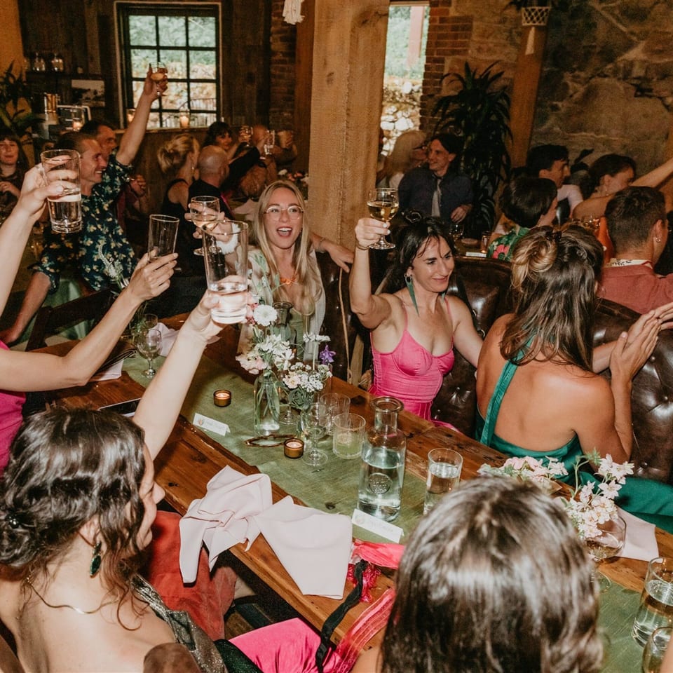 Guests at Stone House restaurant raise glasses in a toast, celebrating in a lively, rustic setting.