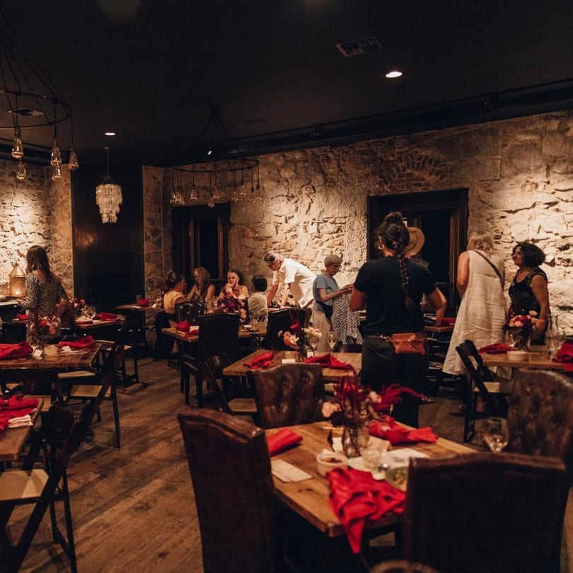 Stone House restaurant interior with guests dining at wooden tables with red napkins and stone walls.