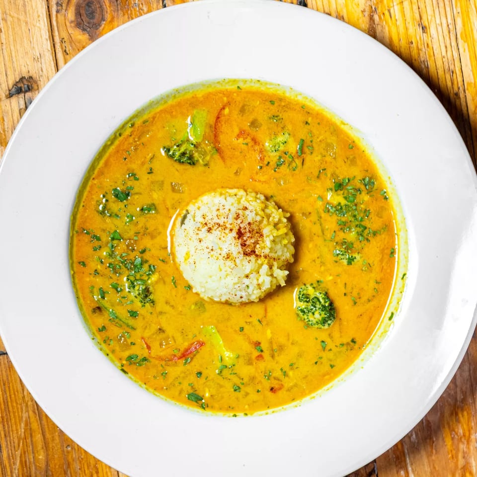 Stone House's yellow curry with broccoli, red peppers, and a scoop of rice on a wooden table.