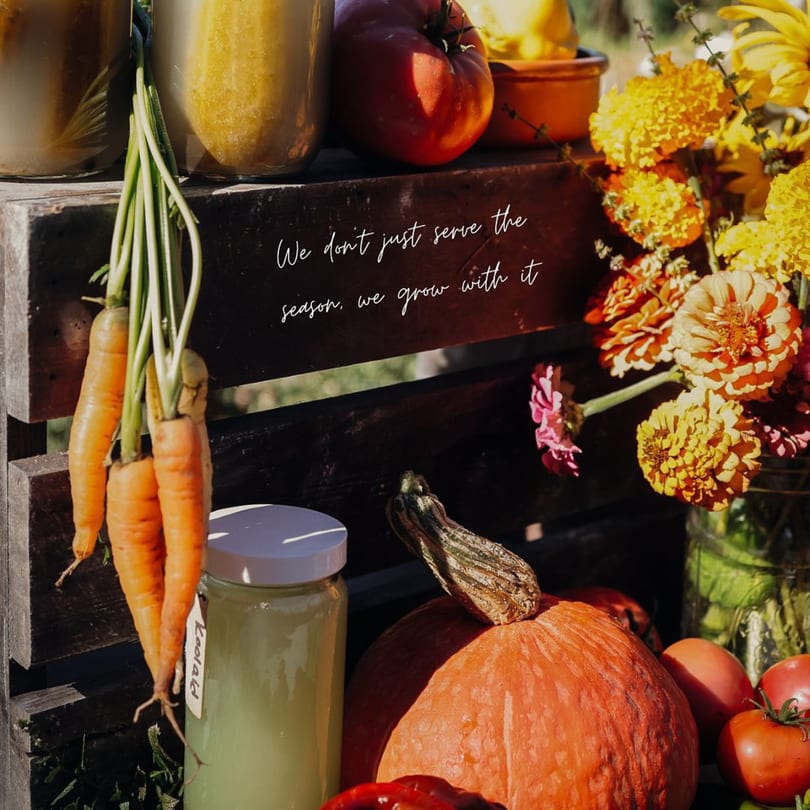 Fresh carrots, tomatoes, pumpkin, and flowers with a quote about growing with the season.