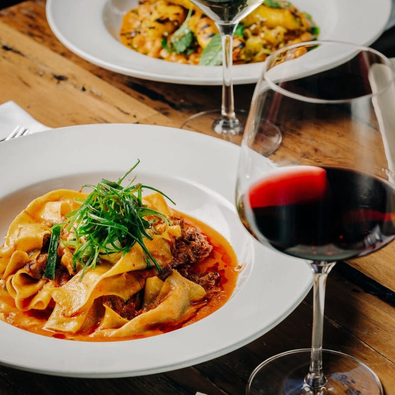 Stone House's pappardelle pasta with rich sauce and greens, paired with a glass of red wine.